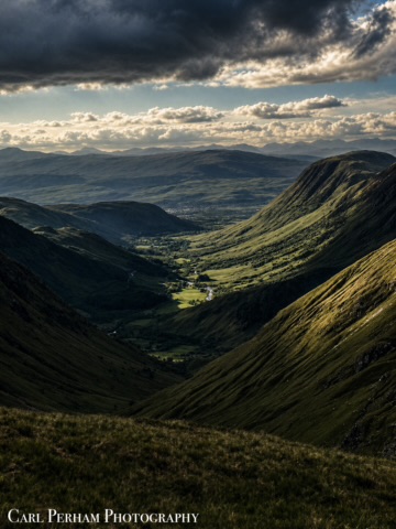 Fort William Valley A scenic valley surrounded by mountains, with sunlight breaking through the clouds.