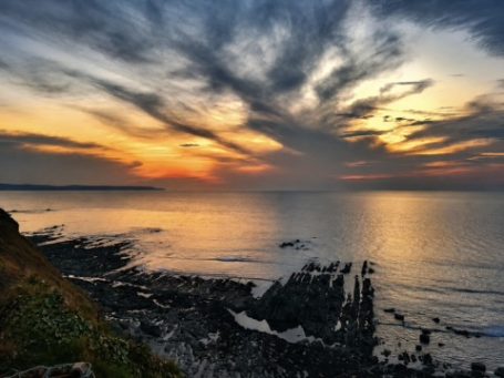 Wacky Ho! Sunset Sunset over calm waters with dramatic clouds and rocky shoreline.