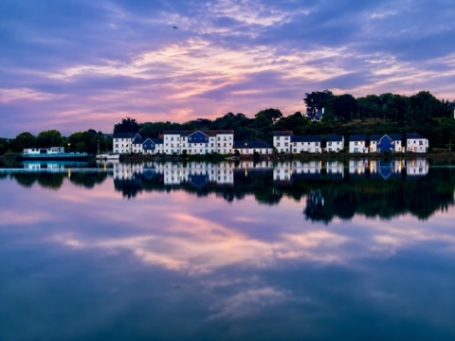 Violet Tide - Bideford Calm lake reflecting colourful sunset and nearby houses.