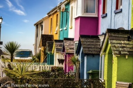 Colourful beach huts lined along a sunny coastline with palm trees in the foreground.