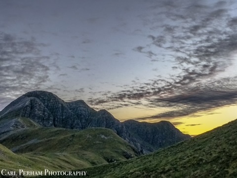 Fort William Sunset over mountain peaks with dramatic clouds and green hills in the foreground.