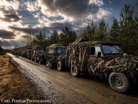 Military vehicles camouflaged and parked along a dirt path in a forested area.