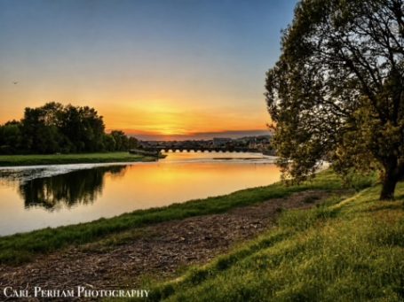 Riverbank Sunset - Barnstaple Sunset over a river with trees and a bridge reflected in the water.