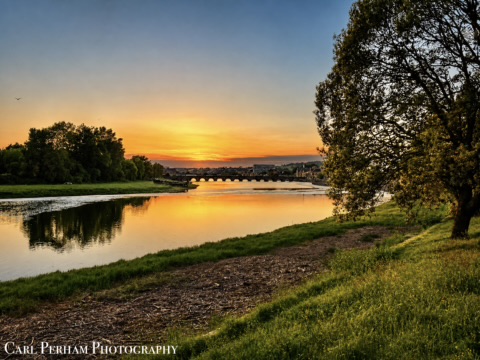 Barnstaple Sunset over a river with trees and a bridge reflected in the water.
