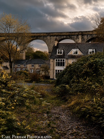 Viaduct Archways A stone viaduct arches over a house, surrounded by autumn foliage and a moody sky.
