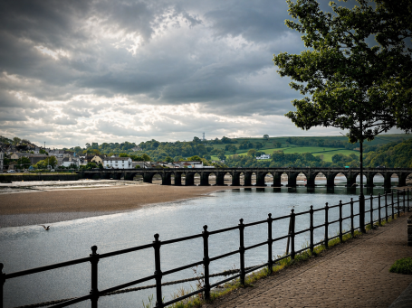 Moody Skies Over Bideford - Bideford A riverside view featuring a stone bridge and overcast skies.