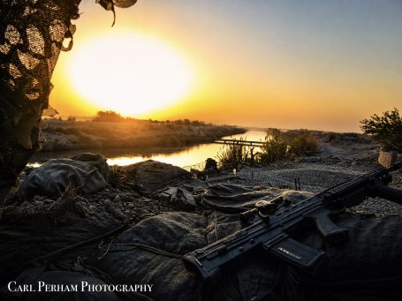 Silhouette of a rifle with a sunset backdrop over a river.