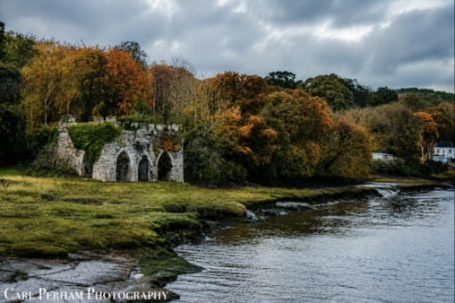 The Silent Ruin - Bideford Historic ruins surrounded by autumn foliage beside a calm river under a cloudy sky.