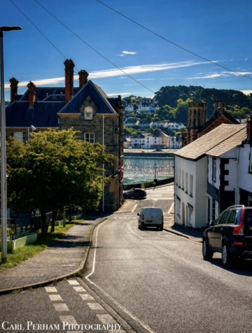 Devon Quiet street winding down towards a body of water, with buildings lining the road.