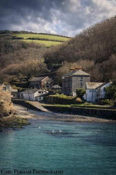 Cornwall Coastal village near water with trees and hills in the background under cloudy skies.